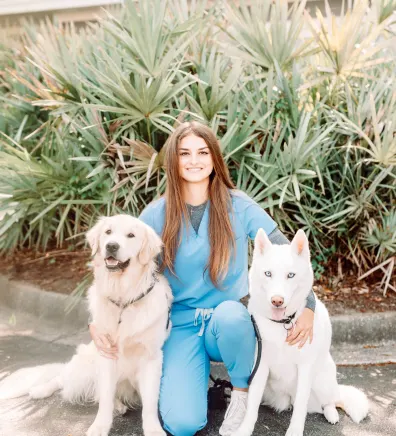 A staff member posing with two white dogs 